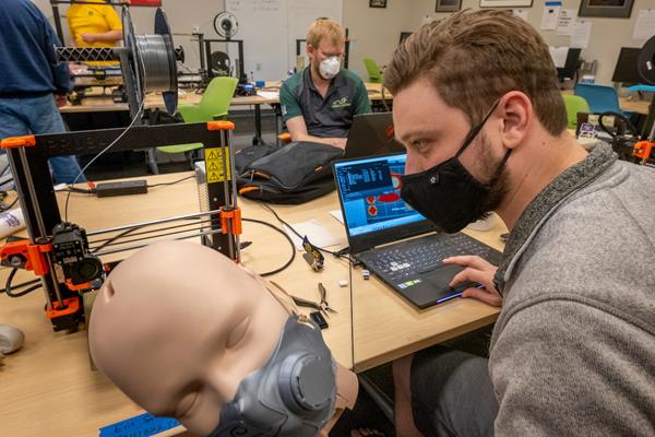 Eric Schneider, a senior aerospace engineering student at Missouri S&T, tests the fit of a prototype 3-D printed surgical mask on the head of a mannequin in the Kummer Student Design Center at S&T. In the background is Stephen Williams, an S&T mechanical engineering student. Photo by Tom Wagner/Missouri S&T. 