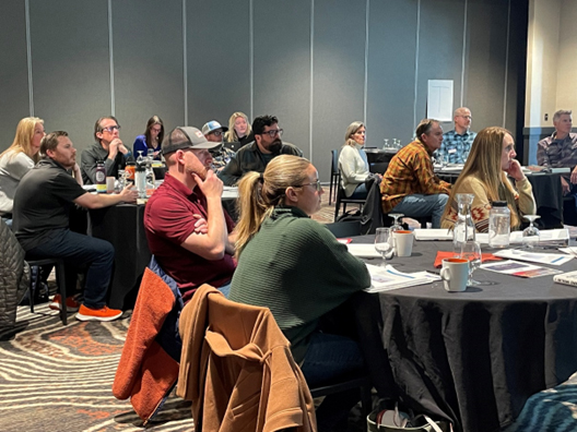 Image shows a group of people seated at several tables taking part in a leadership session