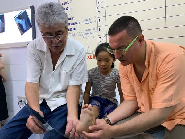 Foot and ankle orthopaedic surgeons, Angel Arnaud, MD, (left) and Altug Tanriover, MD, (right) evaluate the foot of a local Vietnamese child.