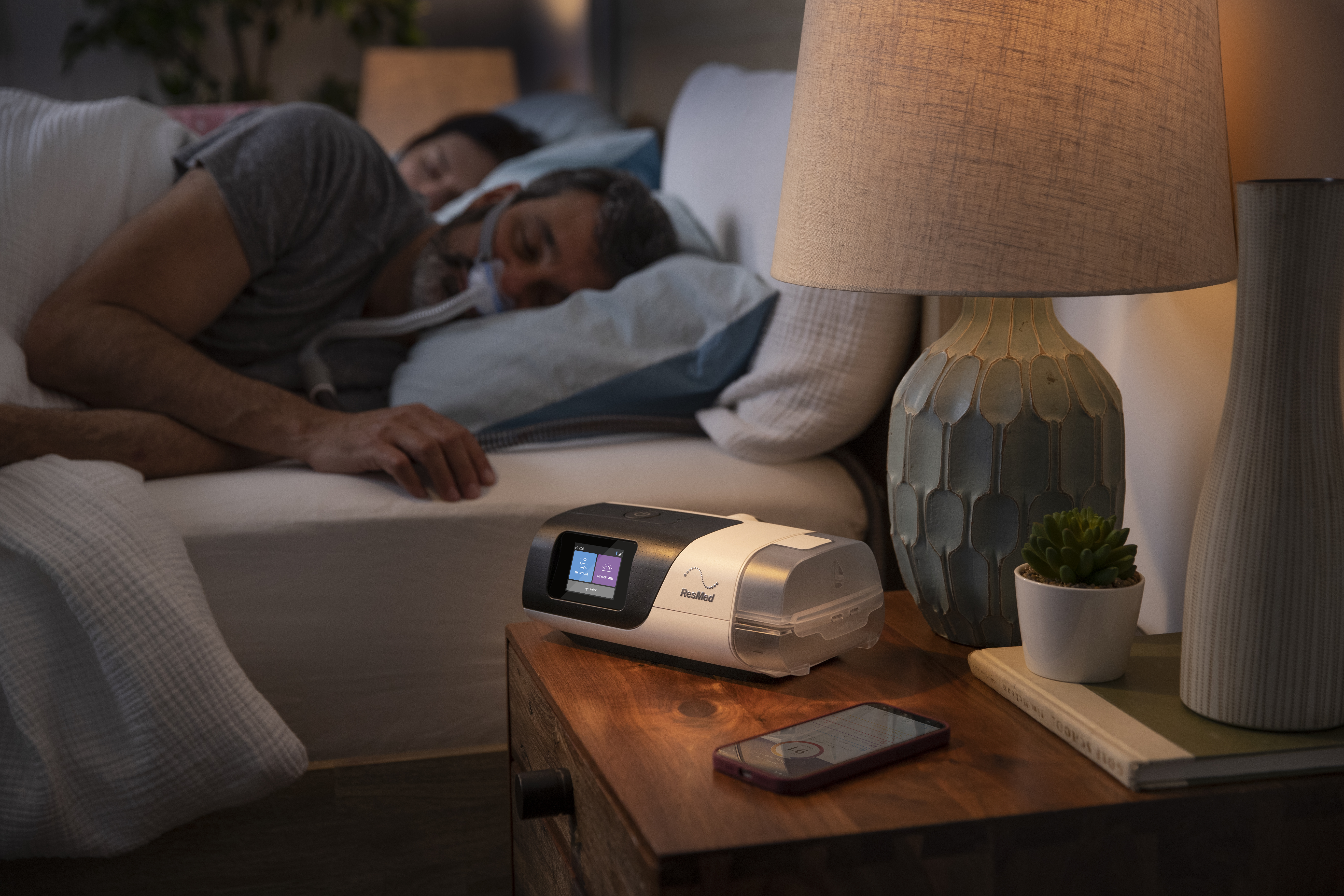 Man Sleeping using Nasal Pillow with AirSense 11 and Phone on Nightstand