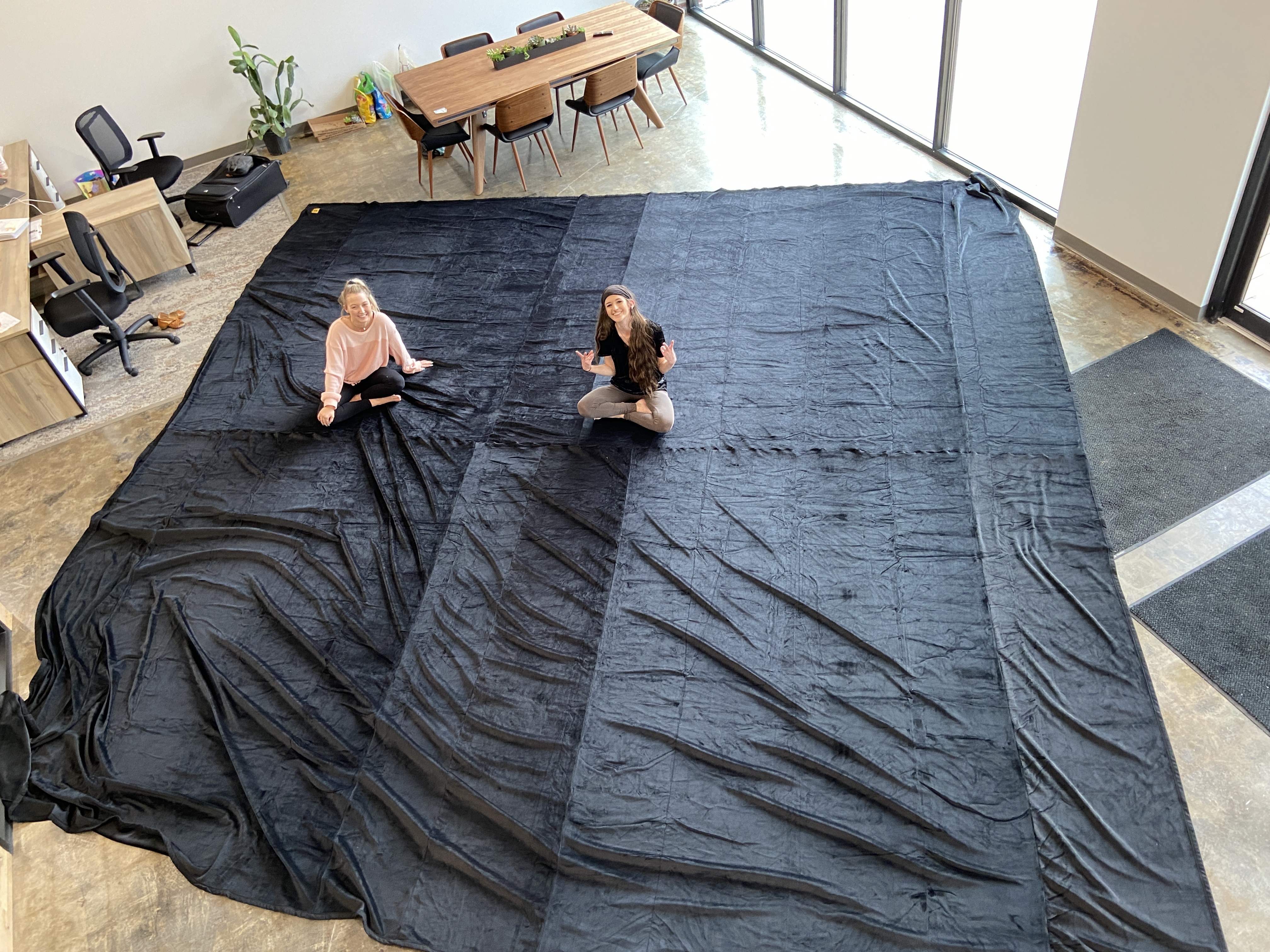 Image shows a 200 square foot blanket covering an entire office floor with two women sitting on the blanket