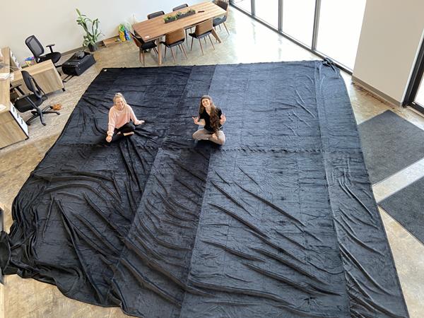 Image shows a 200 square foot blanket covering an entire office floor with two women sitting on the blanket