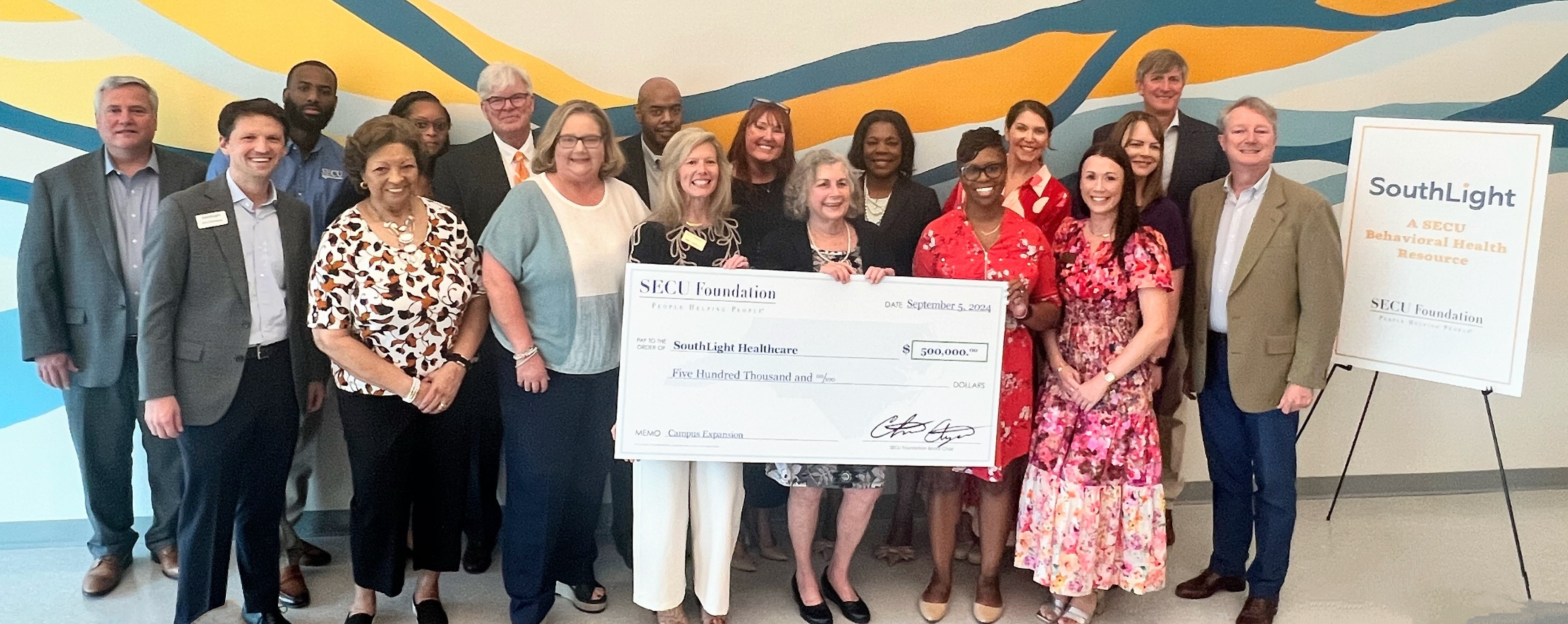 Holding check left to right are SECU Foundation Executive Director Jama Campbell, SECU Foundation Board Member Barbara Perkins, and SECU Branch Vice President Sarah Hill surrounded by SECU, SECU Foundation, and SouthLight Board and staff members.