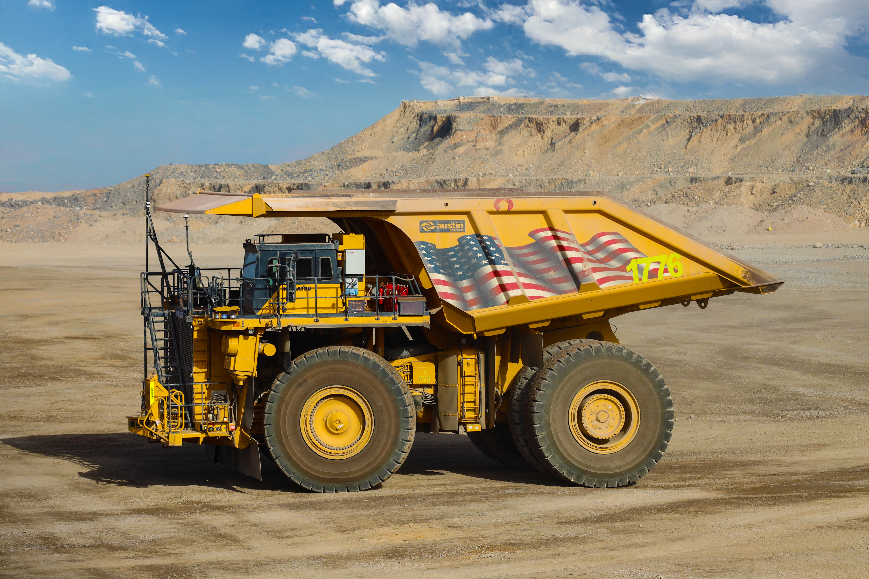 A massive yellow Komatsu haul truck with an enormous dump bed sits on a dirt road at an open-pit mining site in Nevada.