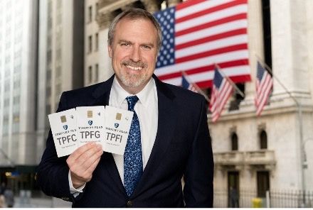 Brian Mumbert holding TPFC, TPFG and TPFI ETF cards in front of the New York Stock Exchange during the Timothy Plan ETF launch