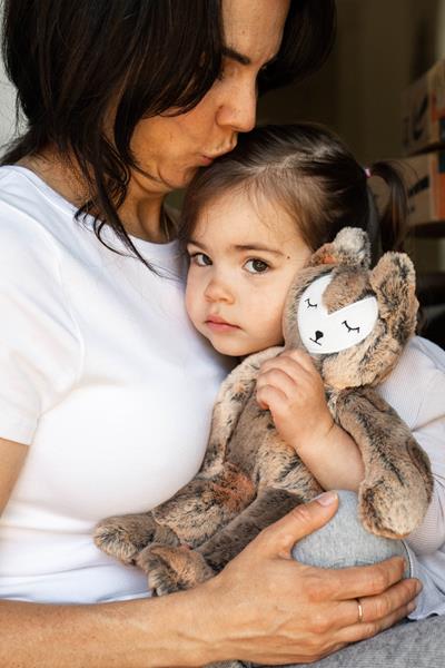 A young girl holds a fox stuffed animal while her mom gives her a hug