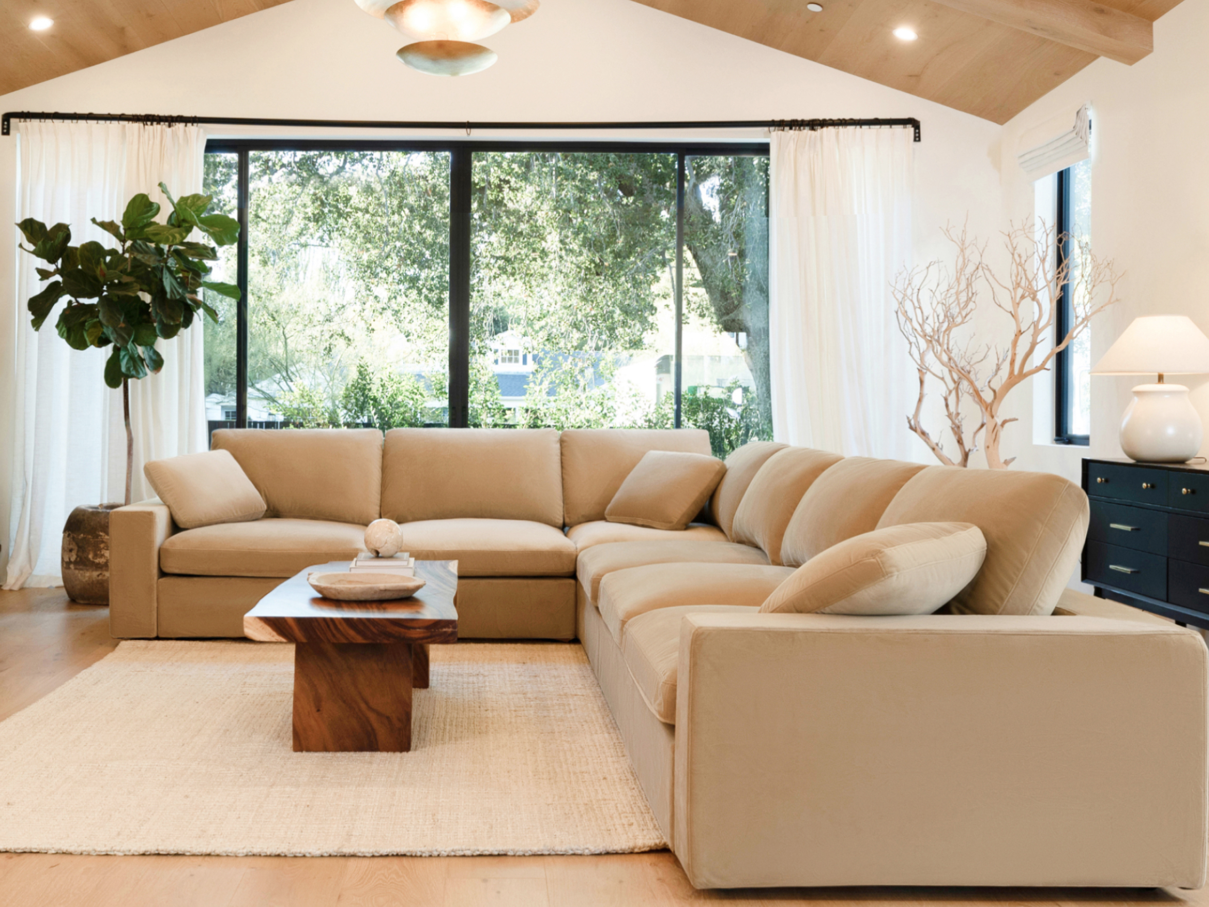 Large Camel Beige modular sectional arranged in an L shape in a bright living room with wood floors and black-framed windows.