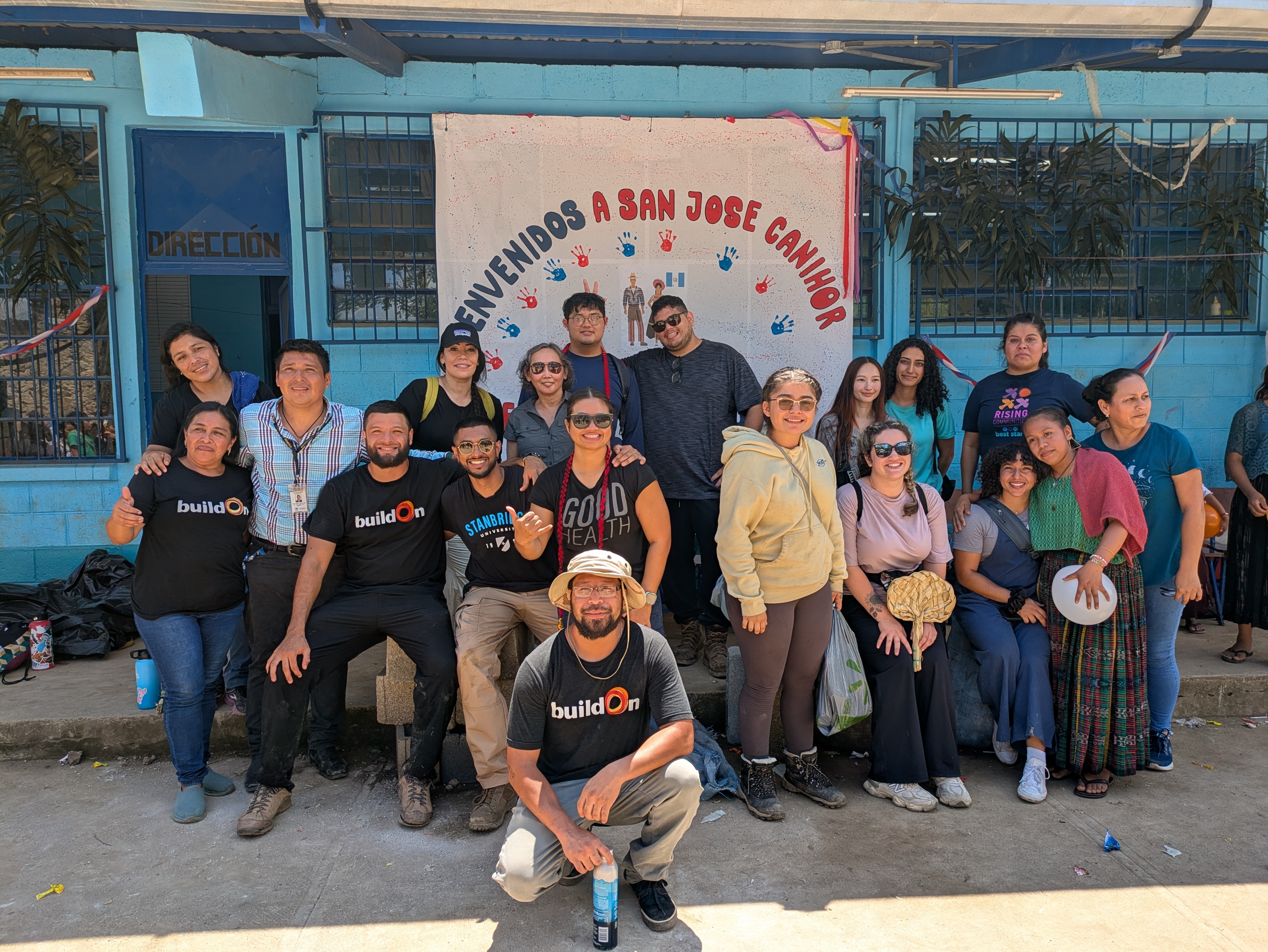 Group of Stanbridge University students, staff, buildOn volunteers, and community members smiling together in front of a welcome banner at the constru