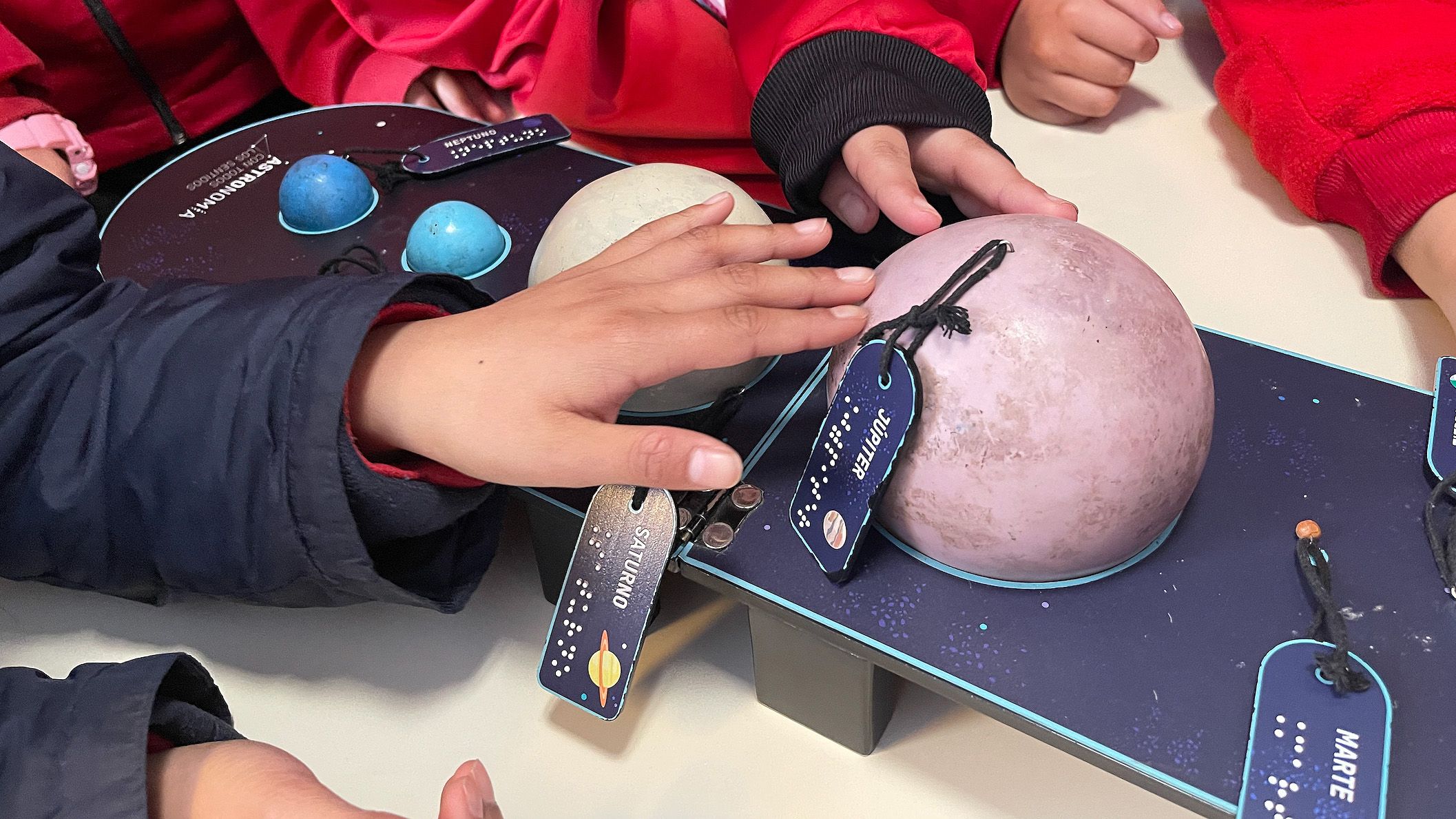 Children in red jackets observe a board displaying a model of the solar system, showcasing their curiosity and engagement.