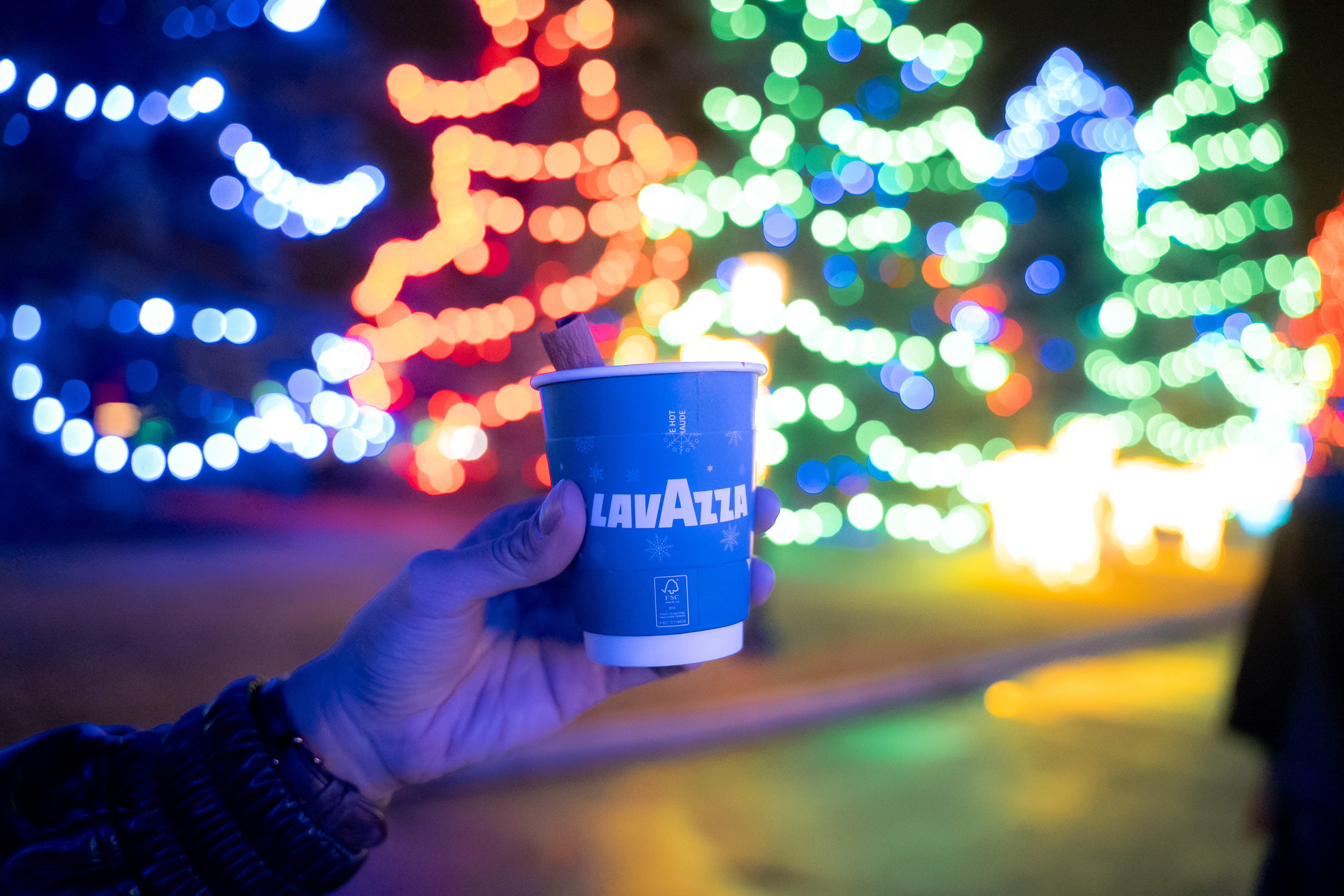Photo of Lavazza coffee cup in hand in front of bokeh holiday lights