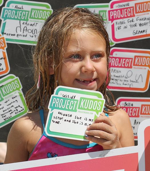 Child holding Project Kudos Sticker. 