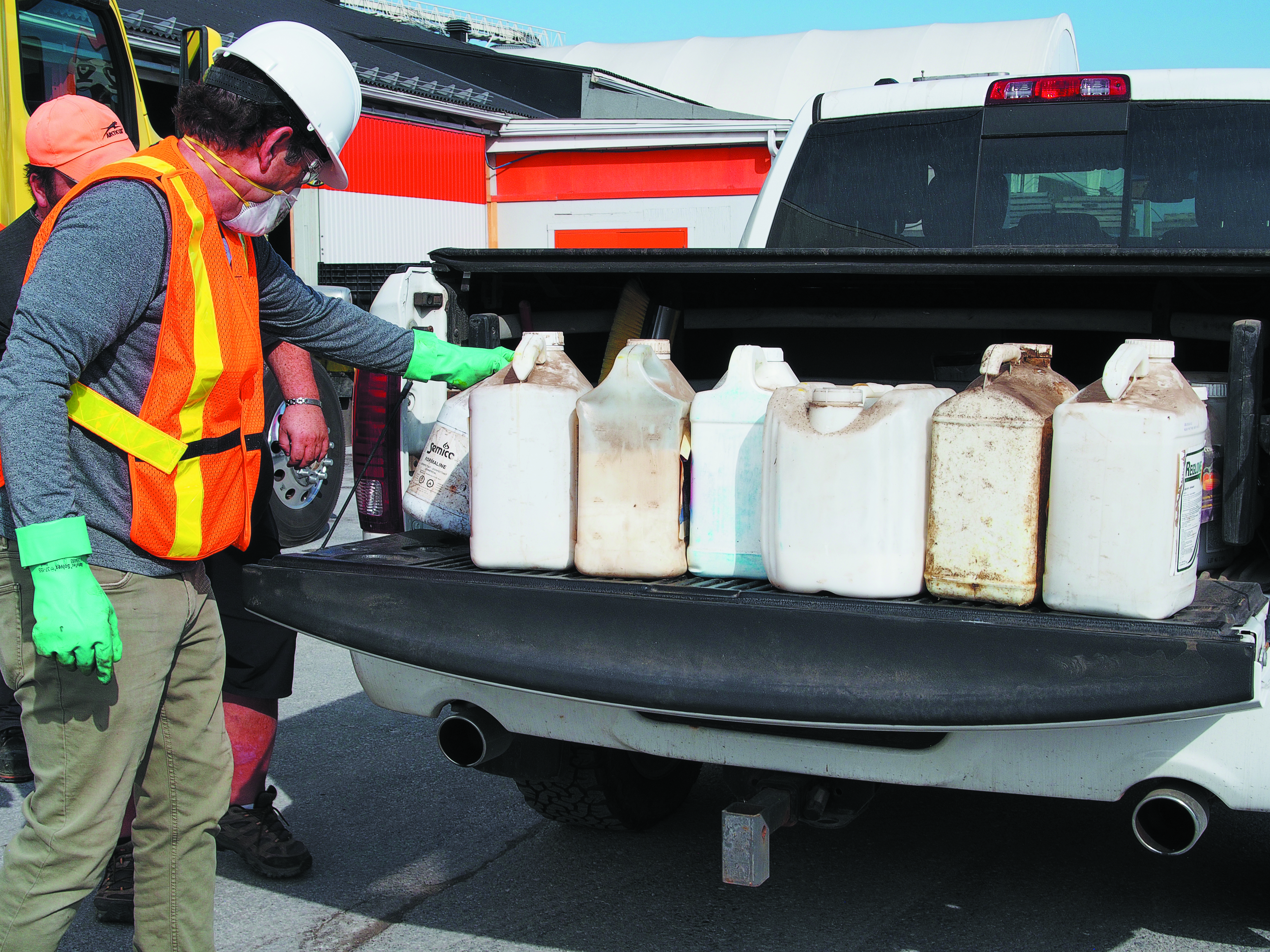 A Cleanfarms contractor wearing PPE, jugs of unwanted agricultural products being being unloaded from the back of a white pickup truck during an event
