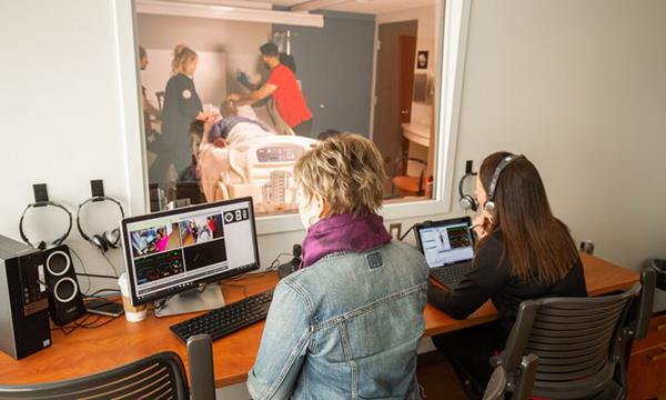 From behind two-way mirrors, Professors Betsy Cambridge (left) and Anita Simmons are watchful but deliberately removed from the students' simulation experience. They use computers to adjust "patient" heart rates and responses to treatments, and they communicate through headsets. 