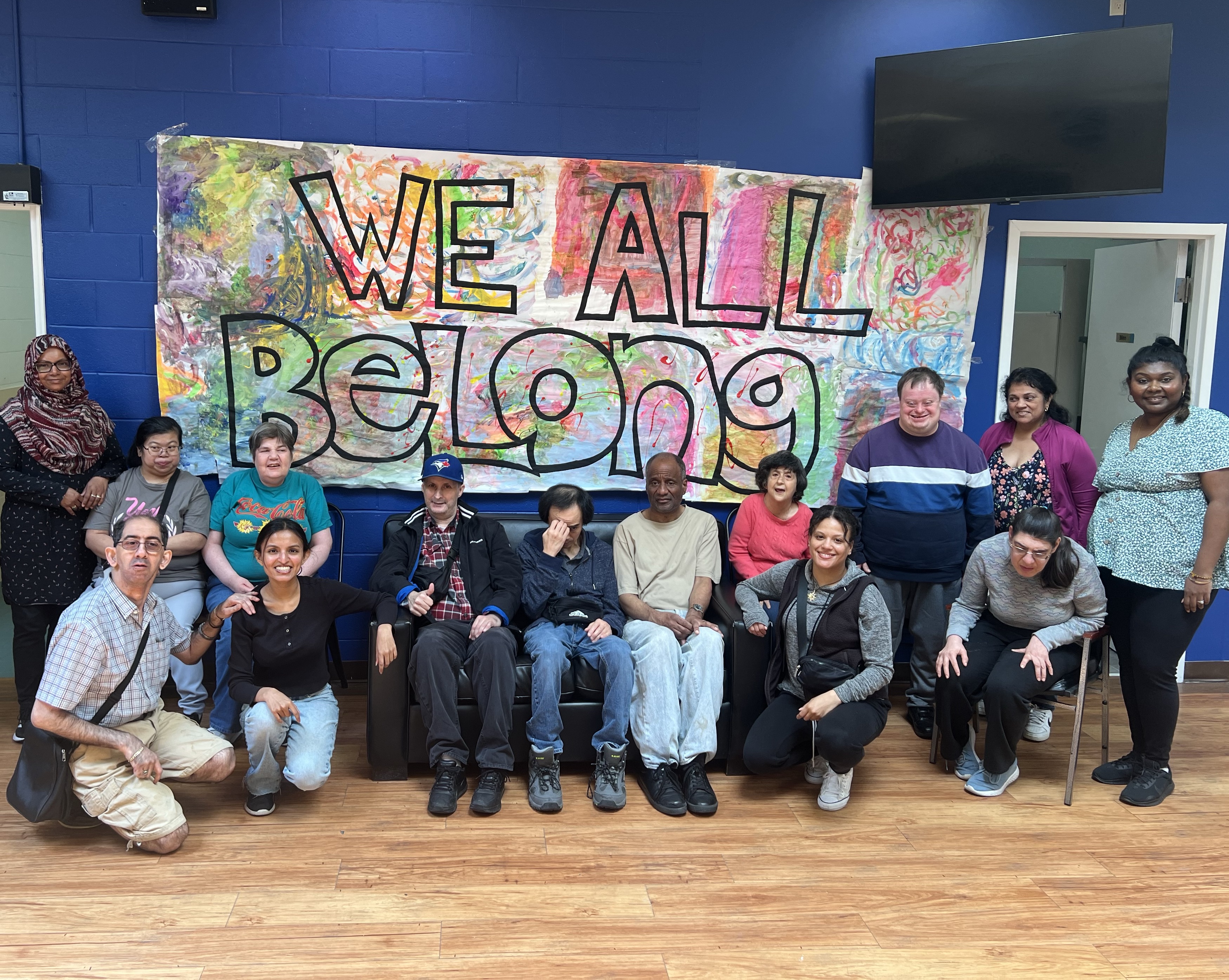 Wrapping up the celebration: people supported by Community Living Toronto gather in front of a handmade ‘WeAllBelong’ sign after a fun event.