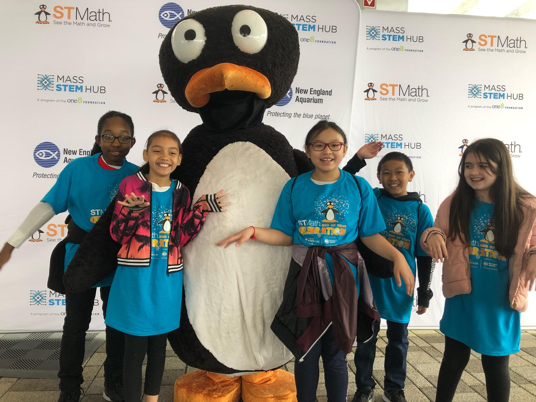 Students strike a pose with JiJi, the loveable penguin mascot from ST Math, during a celebration at the New England Aquarium.