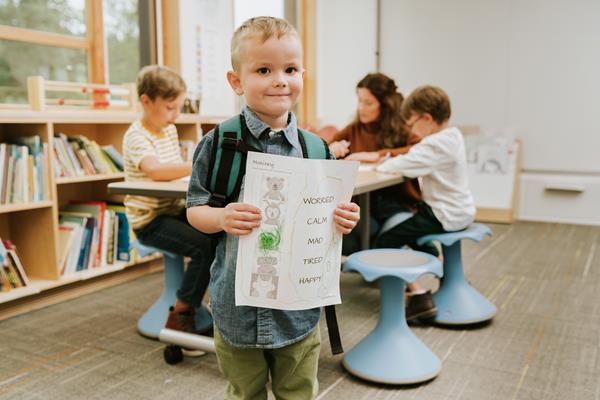 A boy holding a paper that shows his emotions in school.