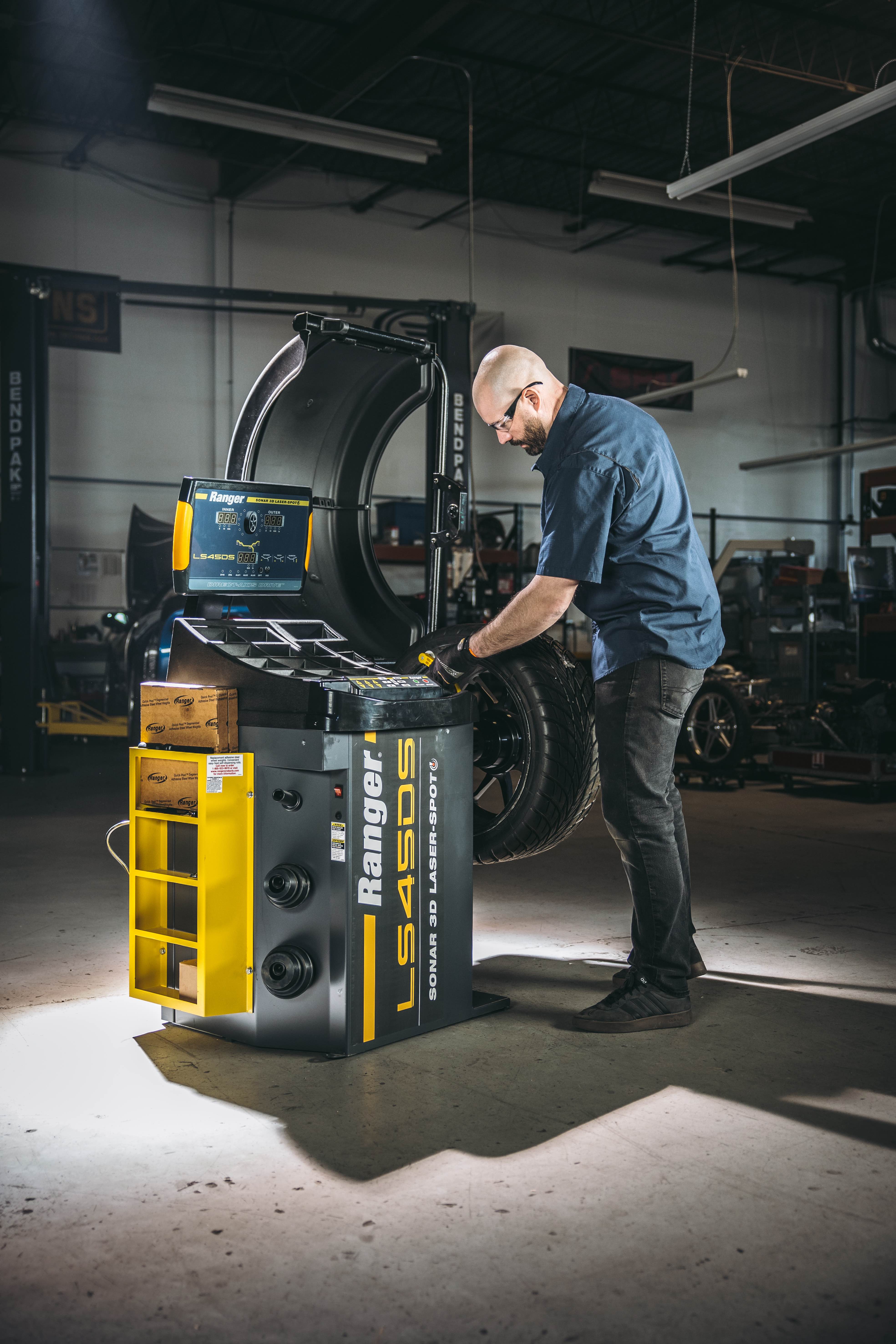 A technician balances a wheel on a Ranger LS45DS Sonar 3D Laser-Spot wheel balancer in an auto repair shop
