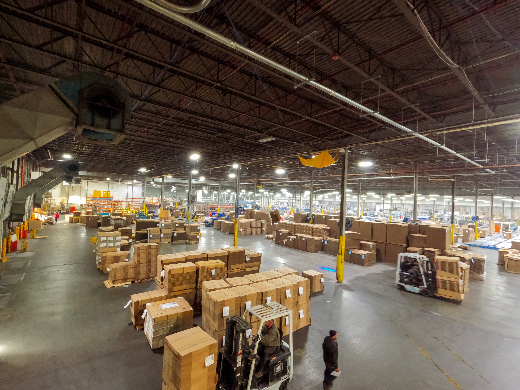 Elevated view of President Container Group's Middletown New York warehouse with forklifts moving pallets of stacked corrugated cardboard boxes ready.