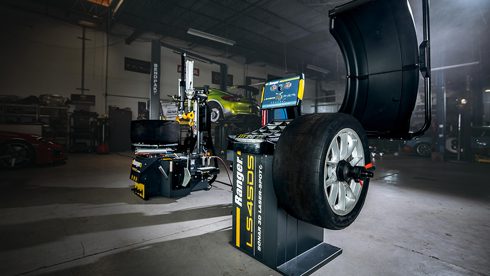 Ranger LS45DS wheel balancer in the foreground of a car repair shop with a Ranger tire changer and BendPak two-post car lift in the background