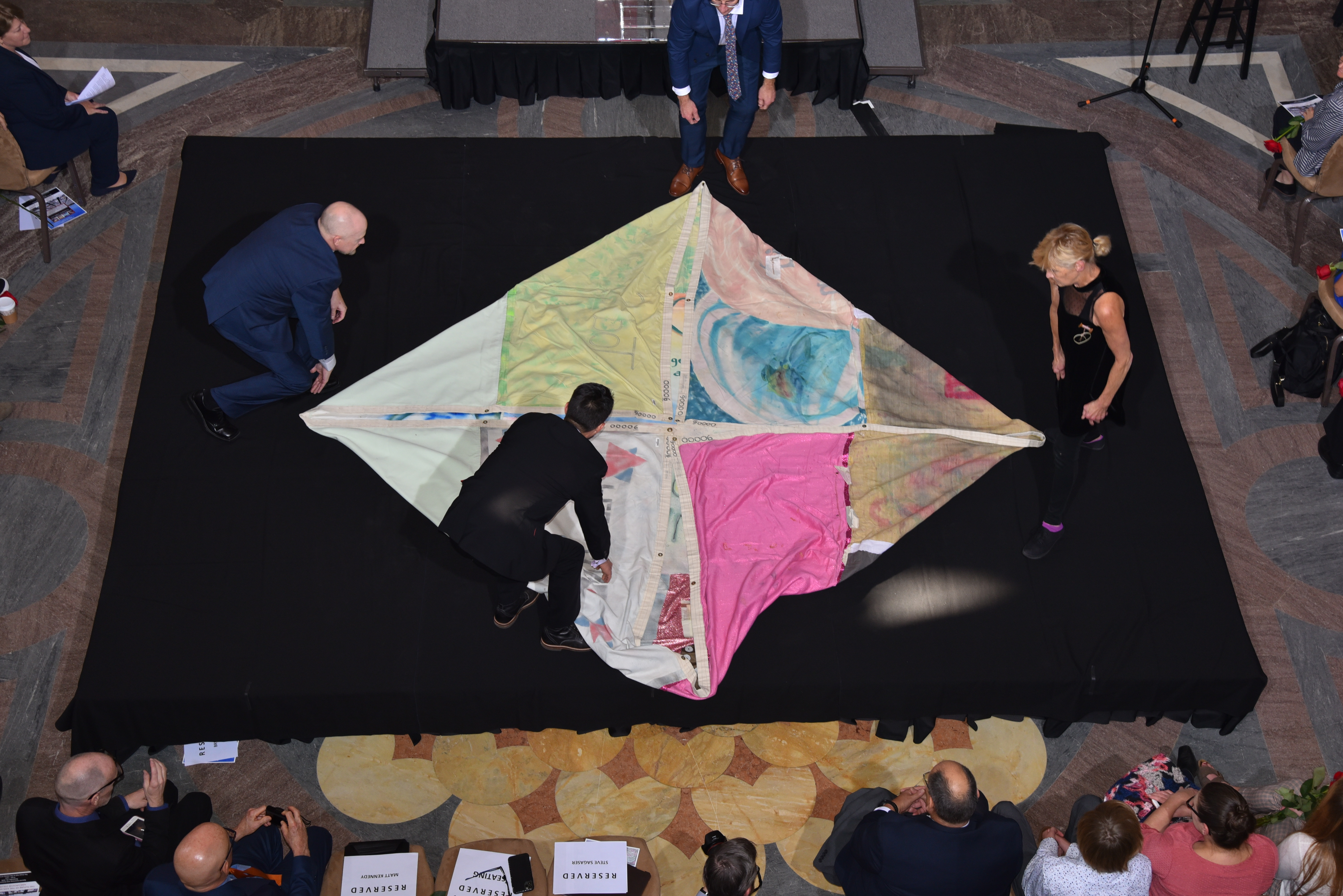 Four individuals ceremoniously unfold one of the first AIDS Memorial Quilt panels ever sewn, memorializing Marvin Feldman at a special event announcing the return of the historic AIDS Memorial Quilt to its original home in San Francisco, where 32 years ago during the height of the AIDS epidemic, a group of strangers gathered at a San Francisco storefront to remember the names and lives of their loved ones they feared history would forget and created first panels of The Quilt to remember them. Photo credit: Mike Shriver