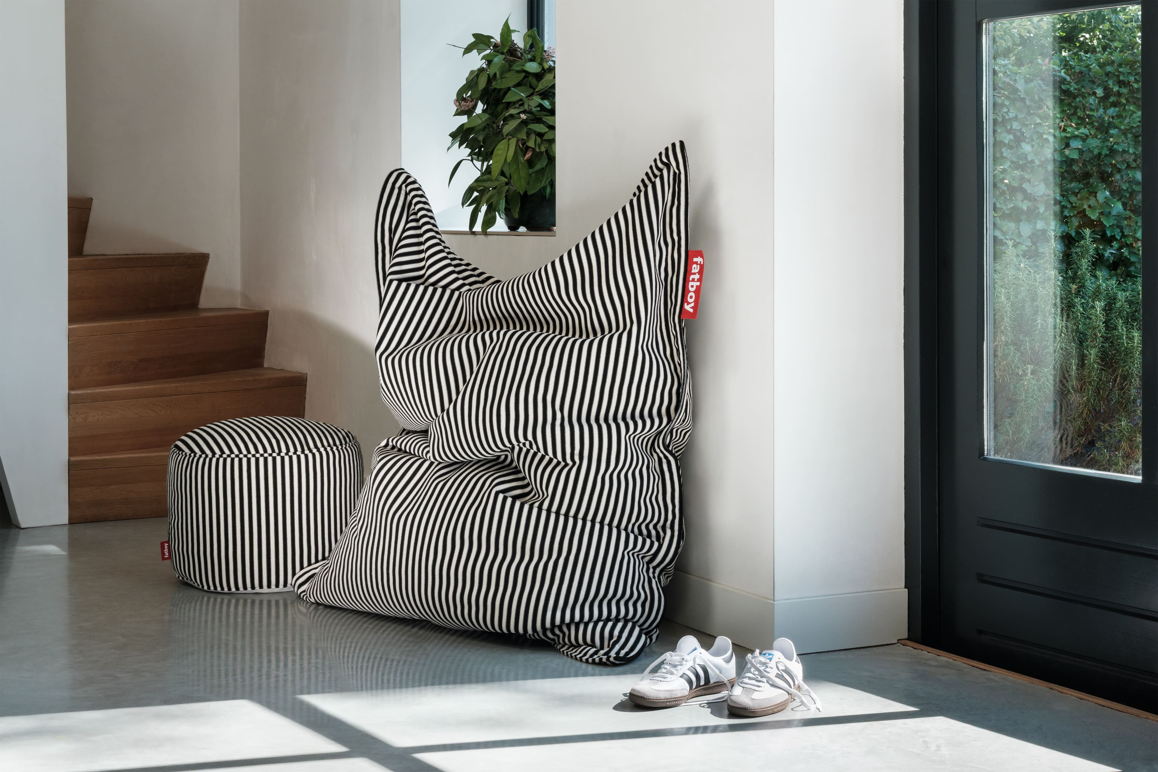 Pouf Slim Terry de Fatboy avec motif rayé noir et blanc, accompagné d’un repose-pied assorti, placé près d’un escalier moderne et d’une porte vitrée.