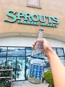 Bottle of Richard's Rainwater sparkling bottled water held up in front of a Sprouts store