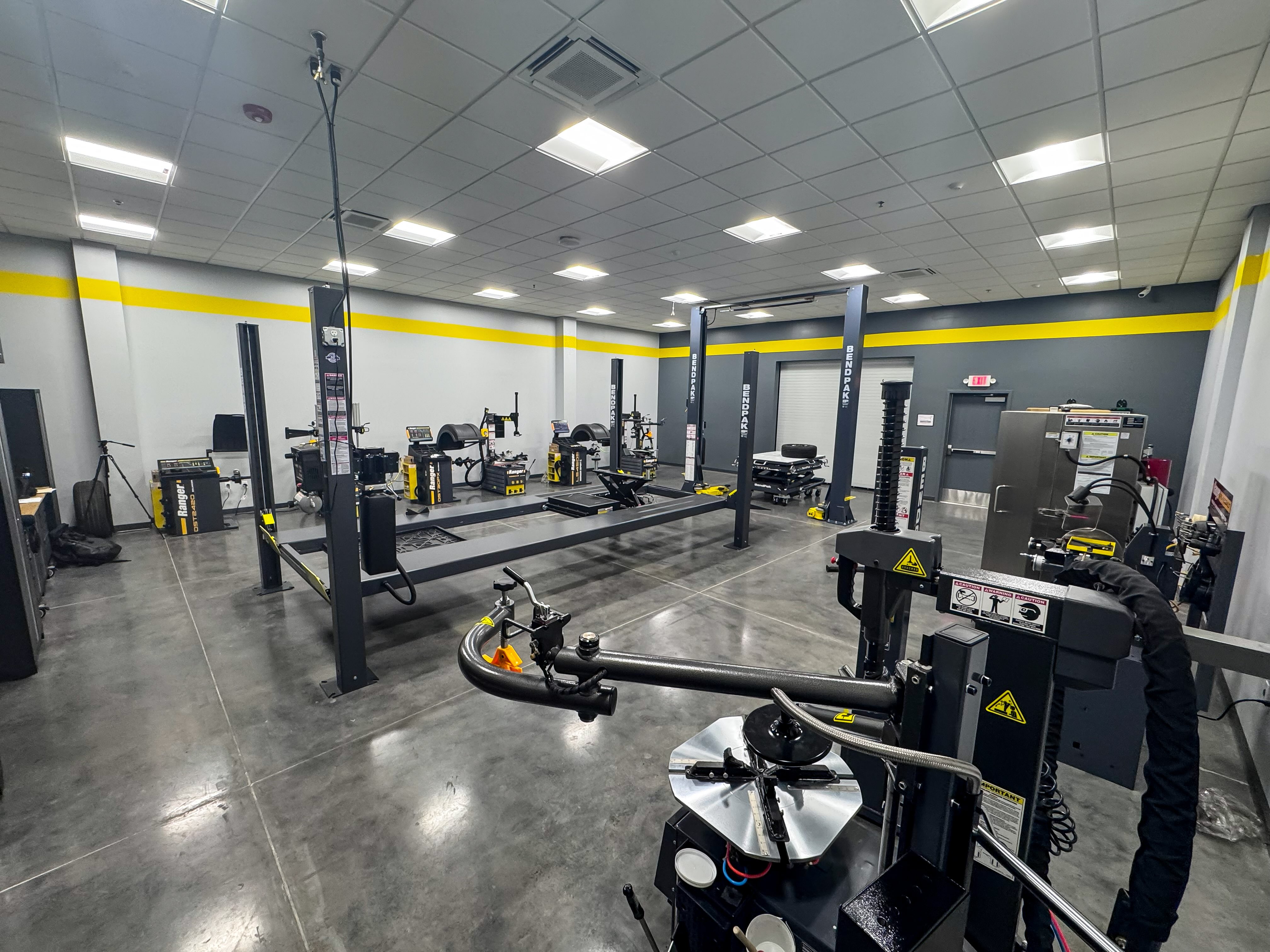 A brightly lit indoor corporate showroom displaying BendPak automotive lifts and Ranger professional service equipment.