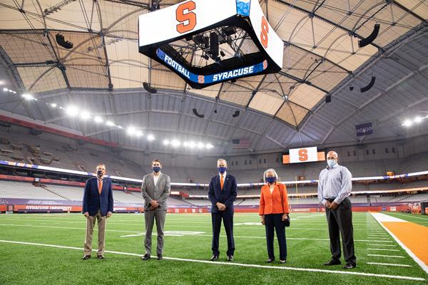 (From L to R) Syracuse University Director of Athletics John Wildhack, Syracuse City Mayor Ben Walsh, Chancellor Kent Syverud, Dr. Ruth Chen and Vice President and Chief Facilities Officer Pete Sala stand on the stadium field beneath the new roof and new center-hung video scoreboard. 

Courtesy: Syracuse University
