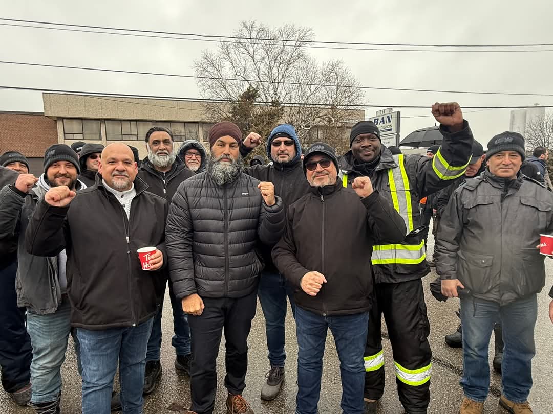 A group of people in winter clothing standing together outdoors, with their fists held up in a so fists held up to show solidarity. 