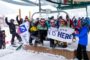 Happy skiers and snowboarders on the first chair break through the opening day banner at Arapahoe Basin