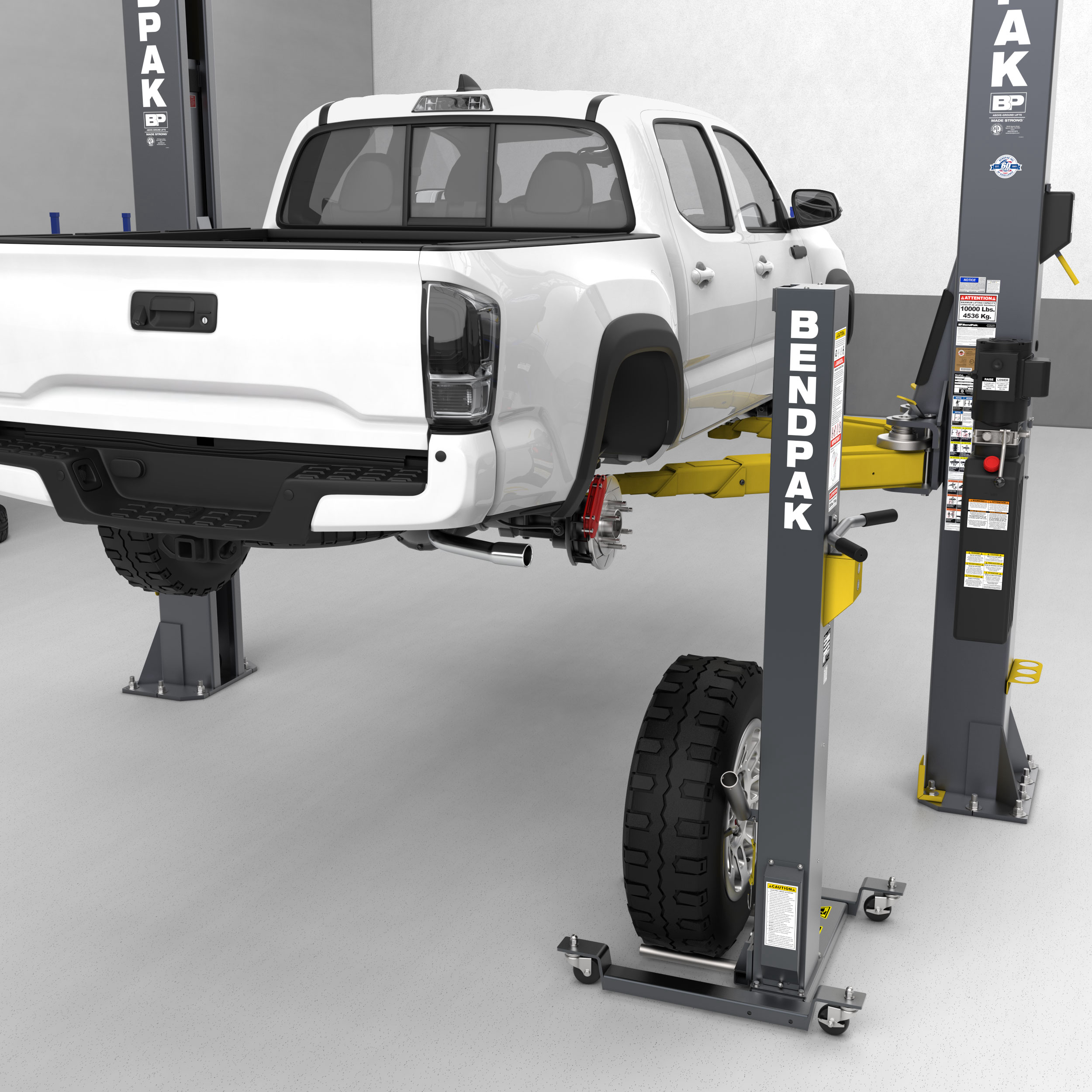 A BendPak mobile wheel lift is positioned to mount a wheel onto a white pickup truck supported by a BendPak two-post lift.