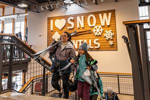 Image shows a woman and a young girl with ski gear they rented that day at Christy Sports