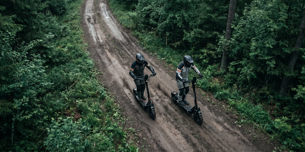 Two riders in full gear cruise ONECNA T2 electric scooters along a muddy forest trail from overhead view