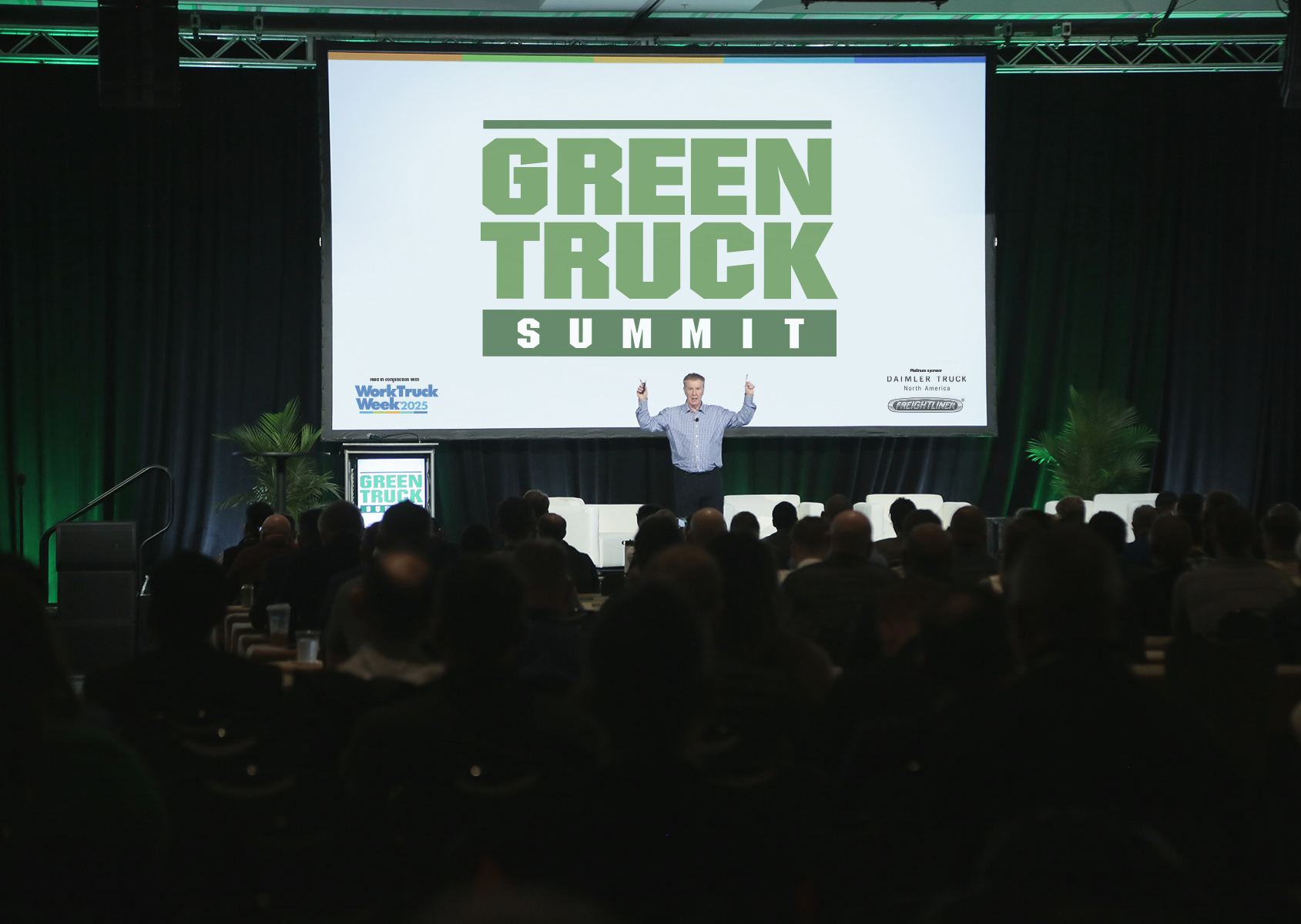 Man on stage pointing to a large screen behind him which say Green Truck Summit