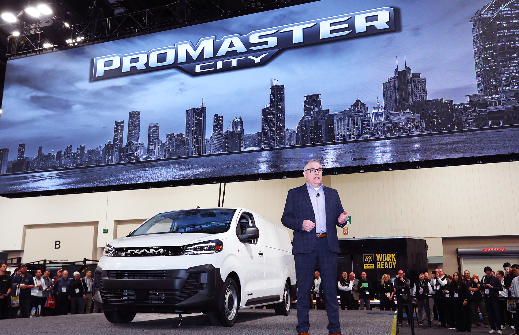 A Ram executive stands on stage next to a white ProMaster City midsize commercial van at Work Truck Week