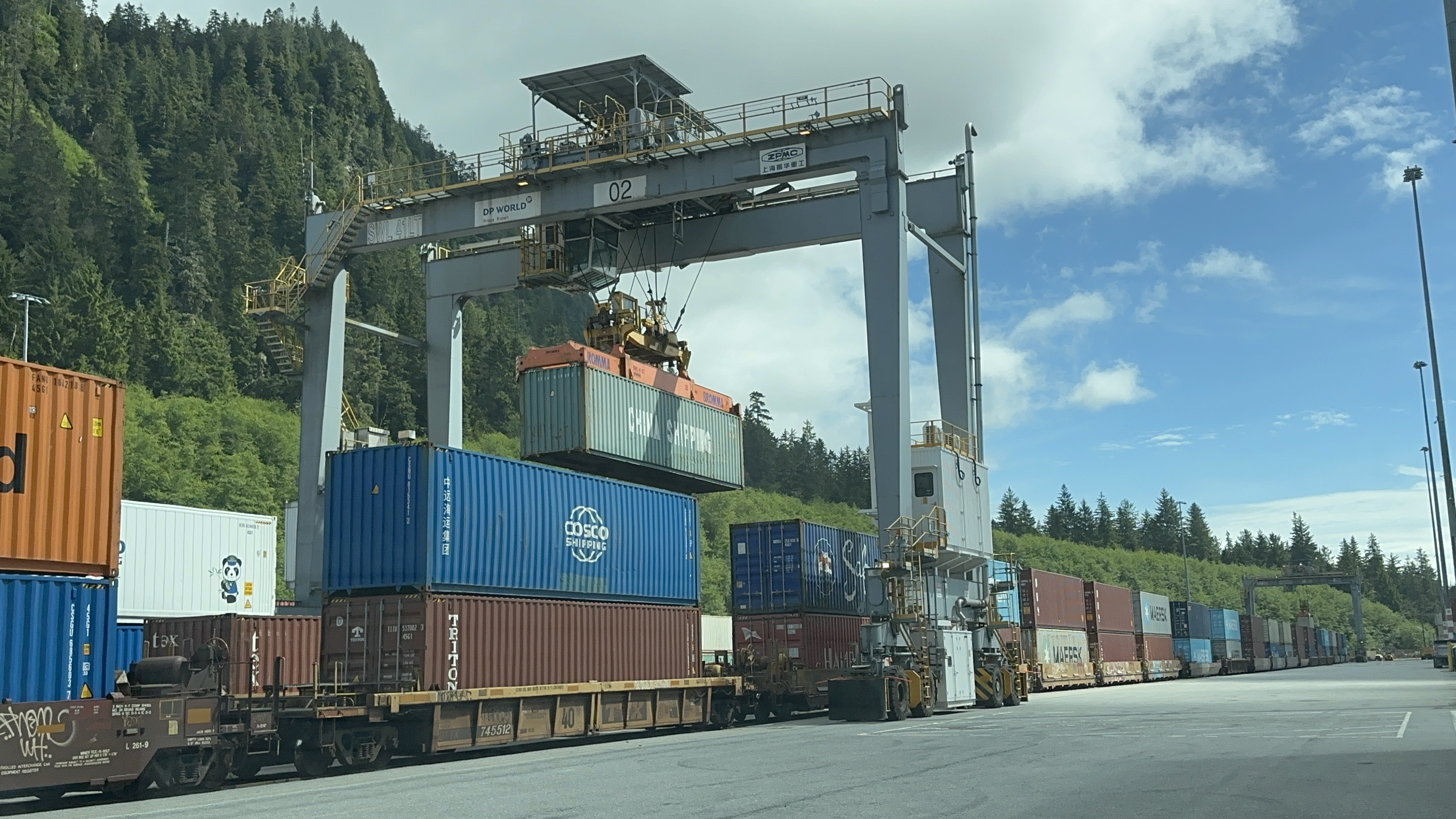 Hybrid RTG crane moving a shipping container above stacked containers and railcars at DP World’s Prince Rupert terminal.