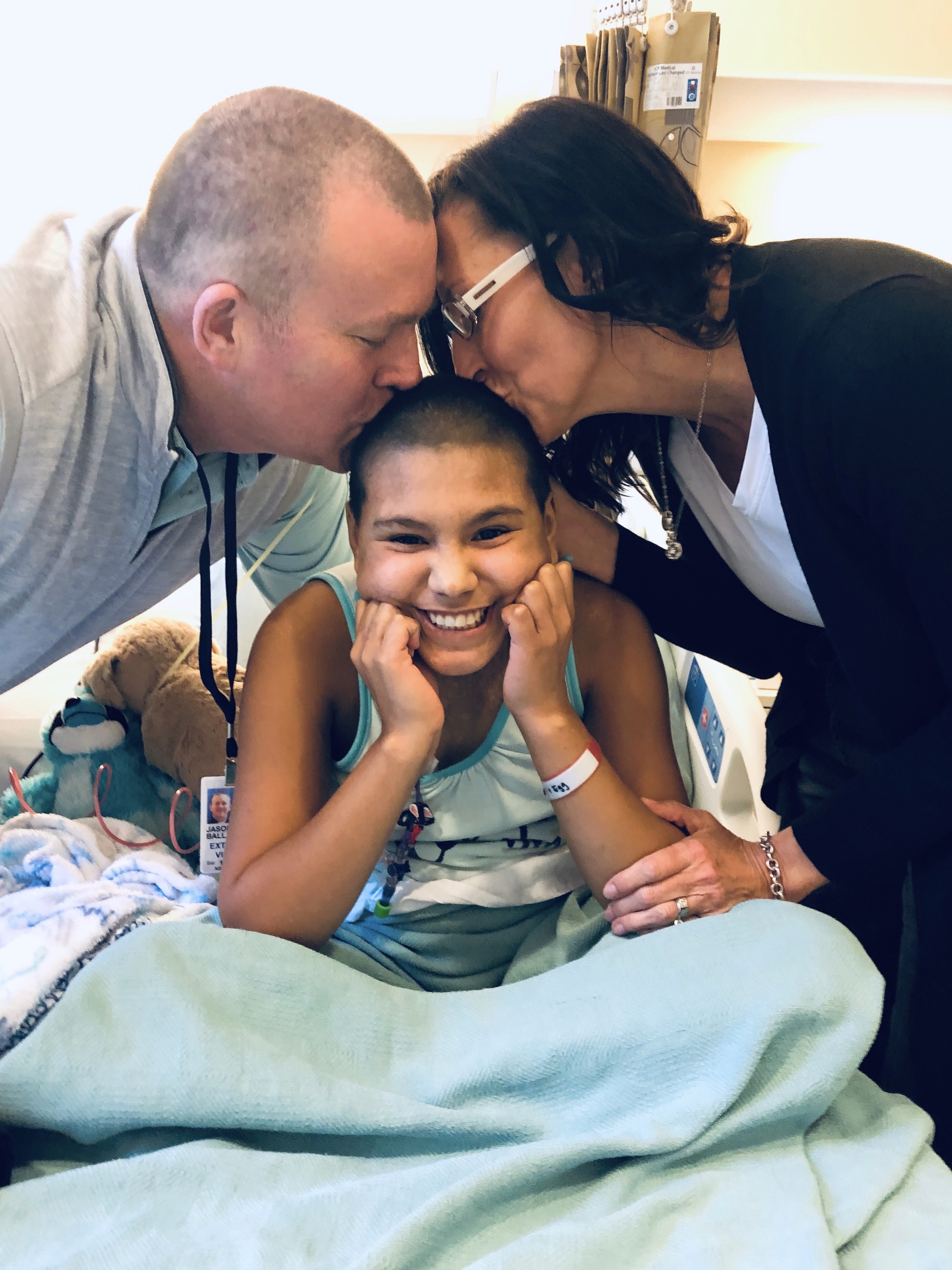 Emi receives kisses from her adoptive parents, Jason and Katie Ballard, at the NIH Clinical Center as she gets ready to receive a lifesaving hematopoietic stem cell transplant, the only way to cure her fatal immune deficiency, using cells donated by her birth mom.