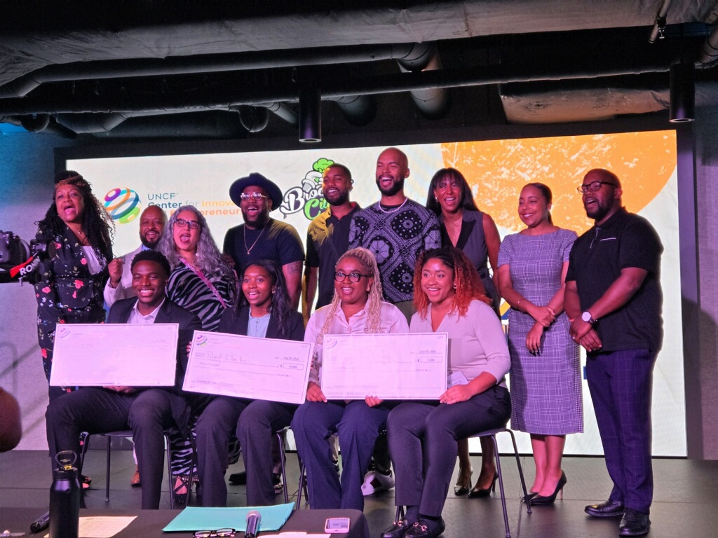 Student entrepreneurs (seated) displaying their winnings with UNCF officials and Center for Innovation and Entrepreneurship staff at Innovate for Impact Pitch Competition hosted by UNCF (United Negro College Fund) at The Gathering Spot in Washington, DC.