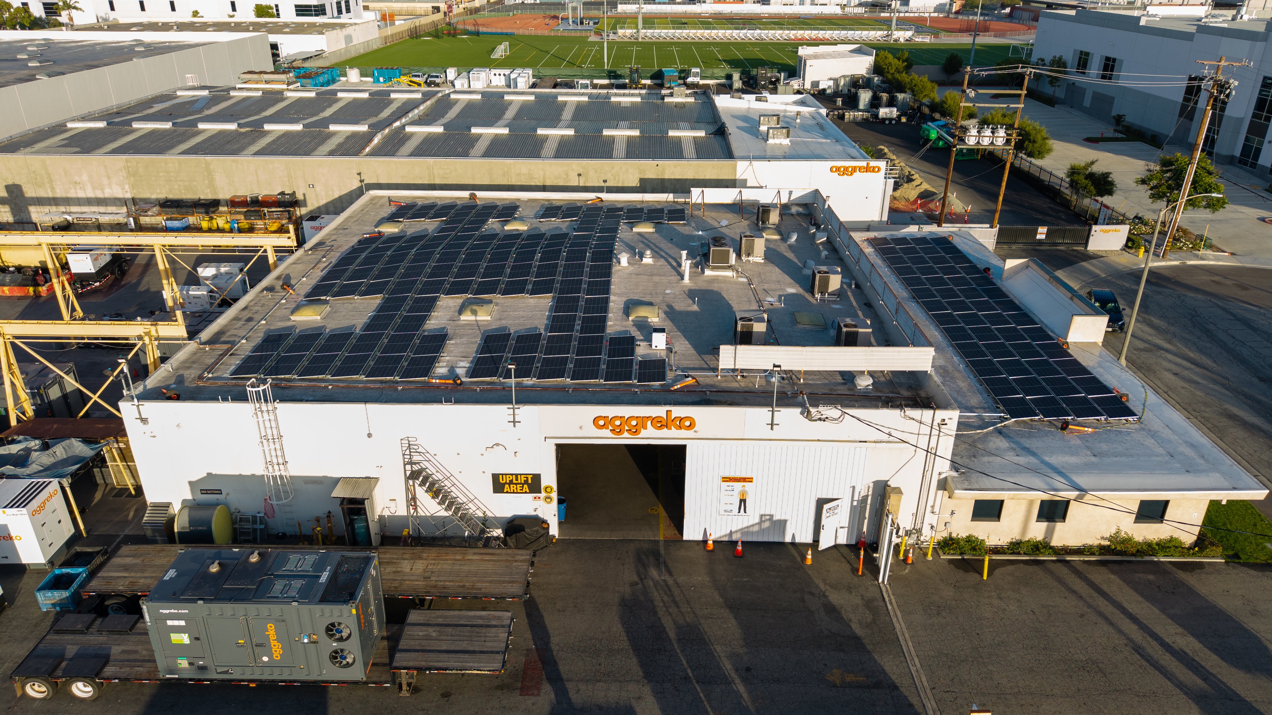 A warehouse in an industrial area with the Aggreko logo on the front and several rows of rooftop solar panels