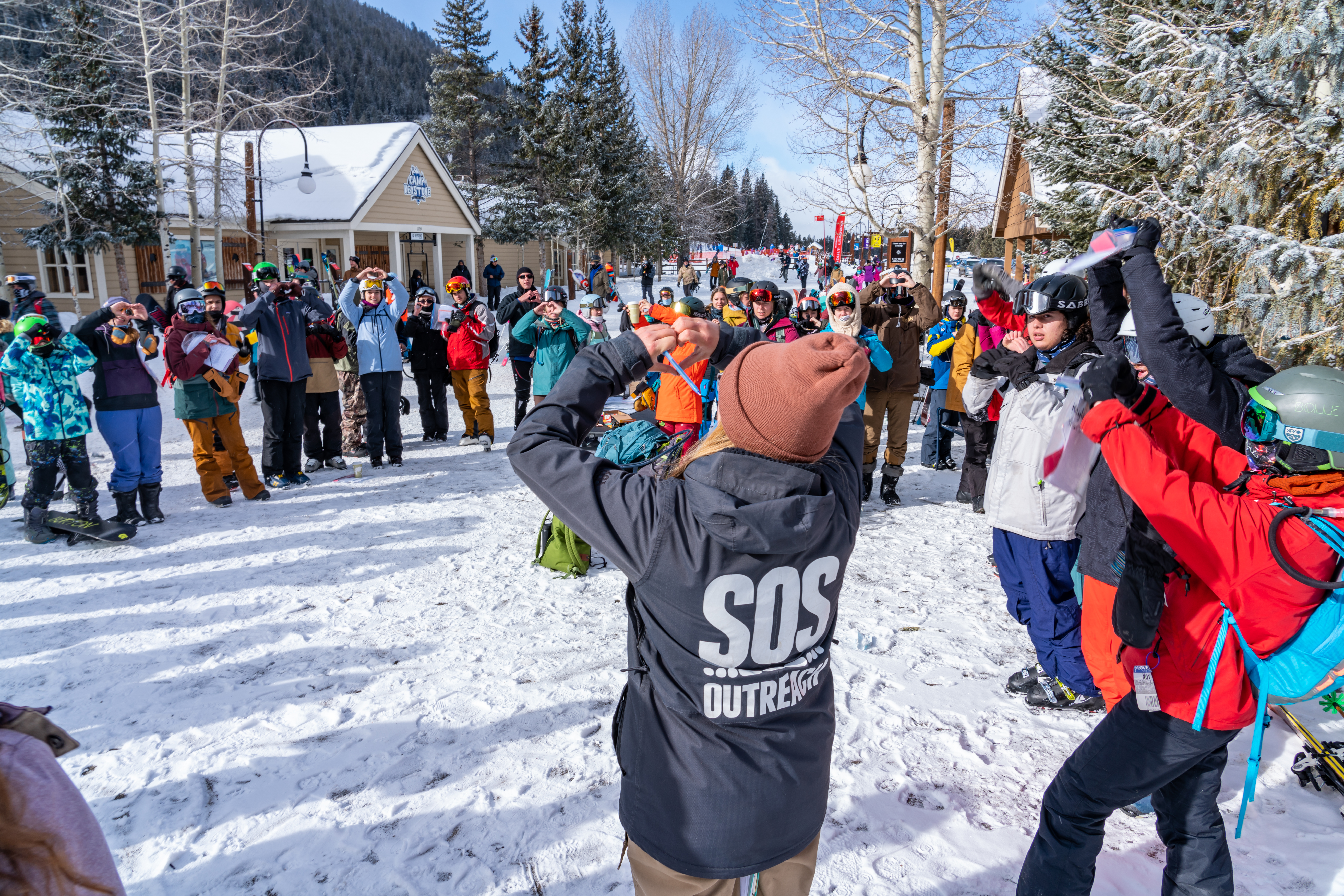 A group of teens in a circle in snow gear holding up heart hands to celebrate the nonprofit SOS Outreach