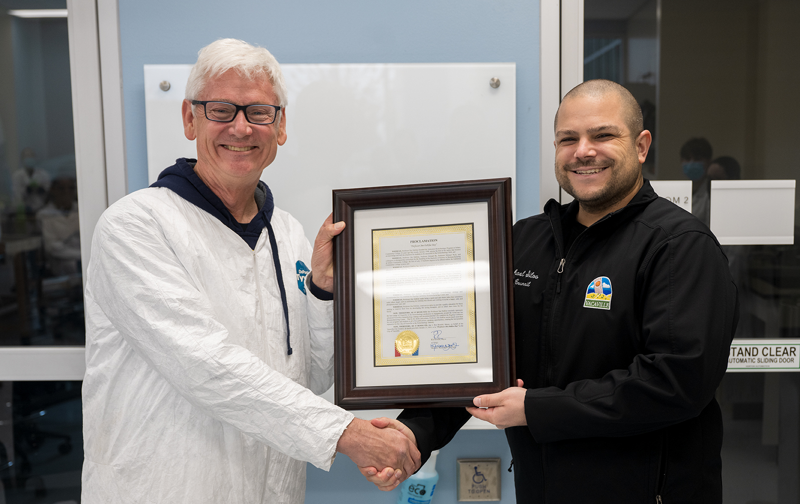 Professor Jim DeKloe and Vacaville Councilmember Michael Silva shake hands holding the proclamation from the City of Vacaville.