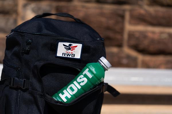 A bottle of HOIST sits in the pocket of a ruck sack with a Team Red, White & Blue patch on it
