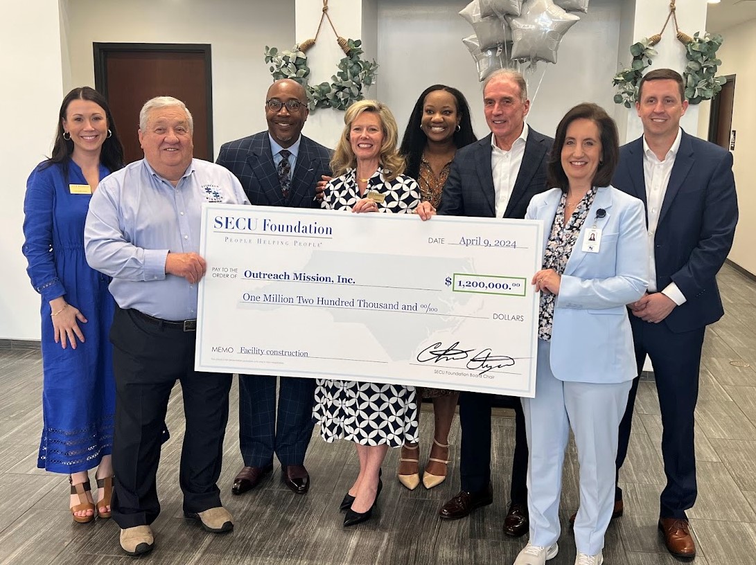 Holding check left to right are Outreach Mission Inc. Board President Hamer Carter, SECU Foundation Executive Director Jama Campbell, SECU Regional Senior Vice President Keith Marion, and Outreach Mission Inc. Executive Director Laura Spivey. Back row left to right are SECU Foundation Vice President Associate Director of Grants Caitlin Duke, SECU Foundation Board Member McKinley Wooten, SECU Sanford Branch Vice President Whitney Clarida, and SECU District Senior Vice President Kevin Watson.
