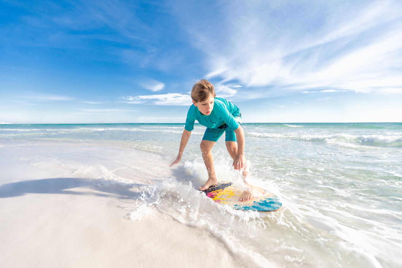 Skimboarding along the white sand beaches of Destin, Florida is one of the many ways beach activities that allow families to enjoy the outdoors while social distancing.