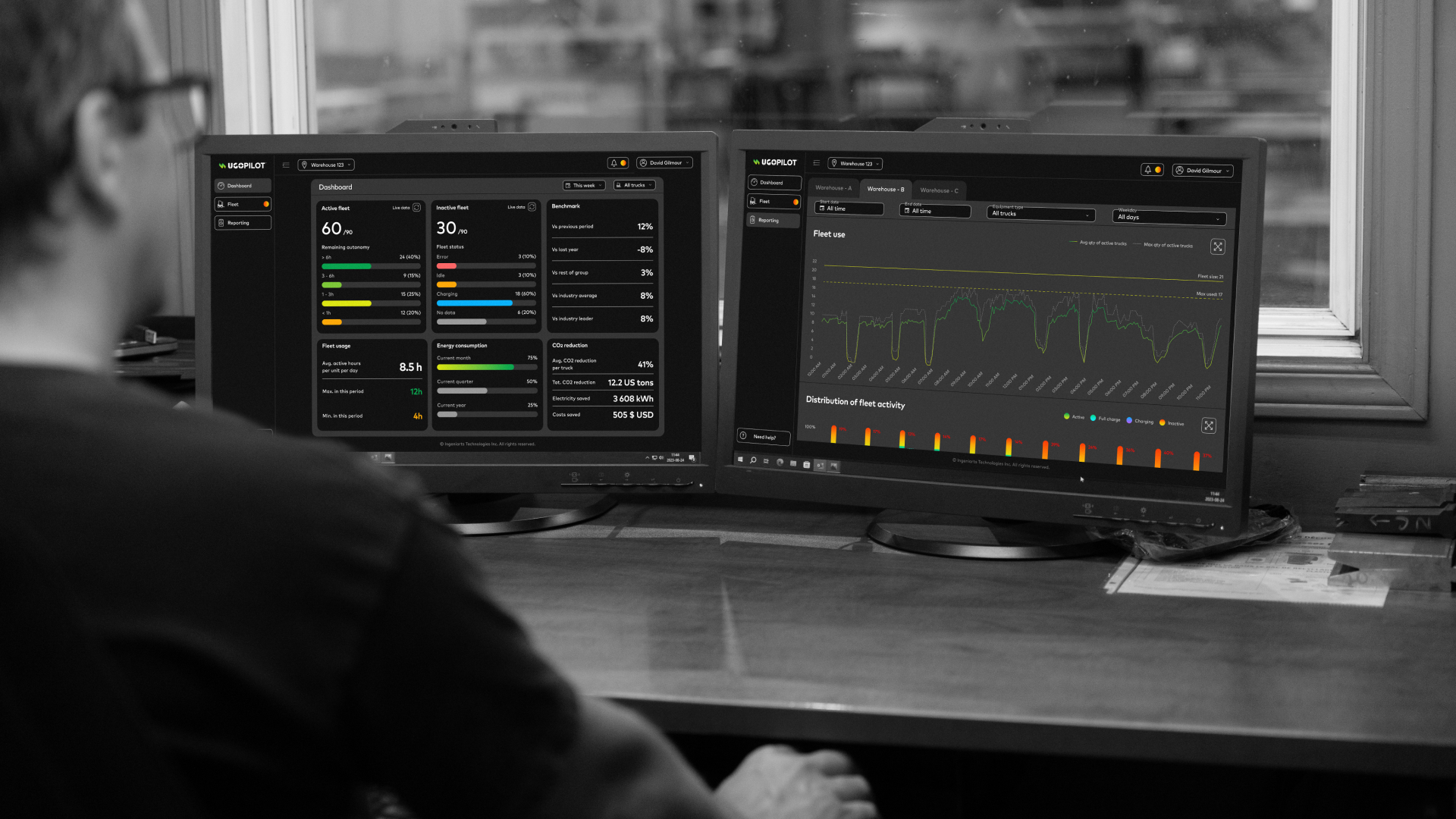 Operations manager looking a two monitors displaying fleet status and operations report by a window on the production floor