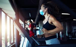 Woman working out at a clean and safe gym in Colorado, wearing a mask on a treadmill.