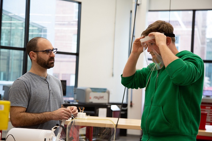 As emergency response teams in the region scramble to acquire dwindling medical supplies to combat the surge in COVID-19 infections, diverse members of the New Jersey Institute of Technology (NJIT) community – from engineers to physicists to advanced manufacturing specialists to students – are designing and fabricating devices to help address the shortfall. 

Here, Justin Suriano and Daniel Brateris try on a face shield they designed and fabricated in the Makerspace at NJIT. 

“Our goal was to build something as cleanly as possible that is easily sanitized and reusable,” said Brateris, director of experiential learning at NJIT’s Newark College of Engineering (NCE).
