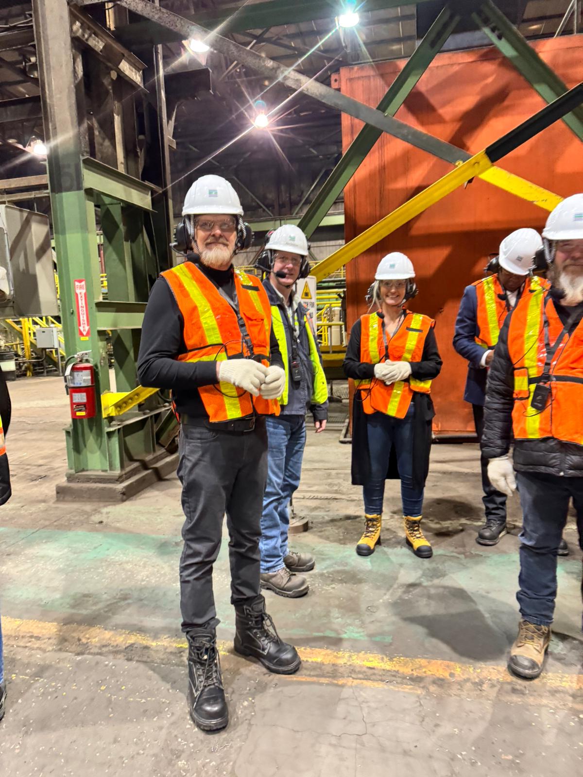 Un groupe de cinq personnes dans un lieu de travail industriel qui portent des gilets réfléchissants, des casques et des chaussures de sécurité.