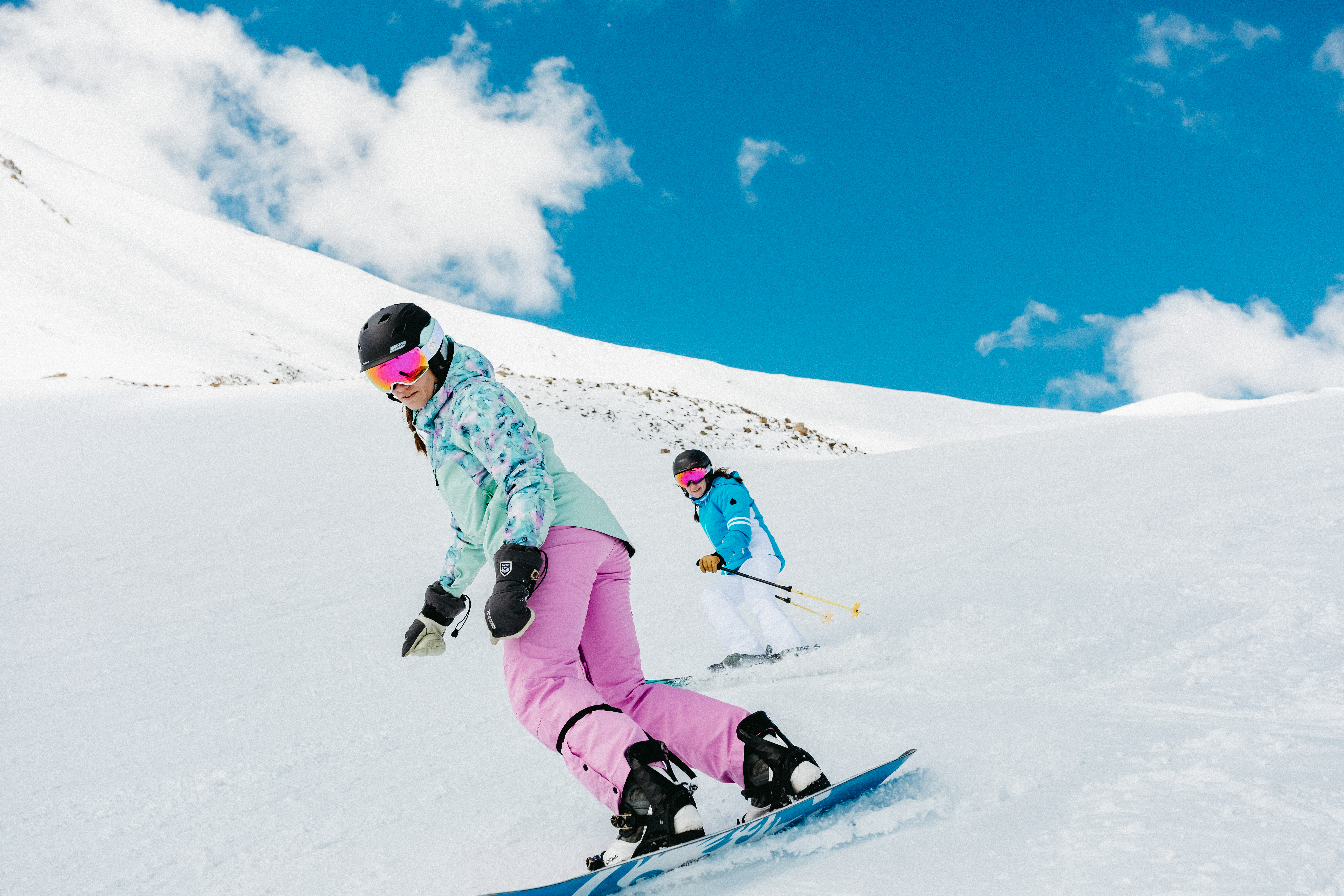 A woman snowboarding and a woman skiing with gear from Christy Sports.