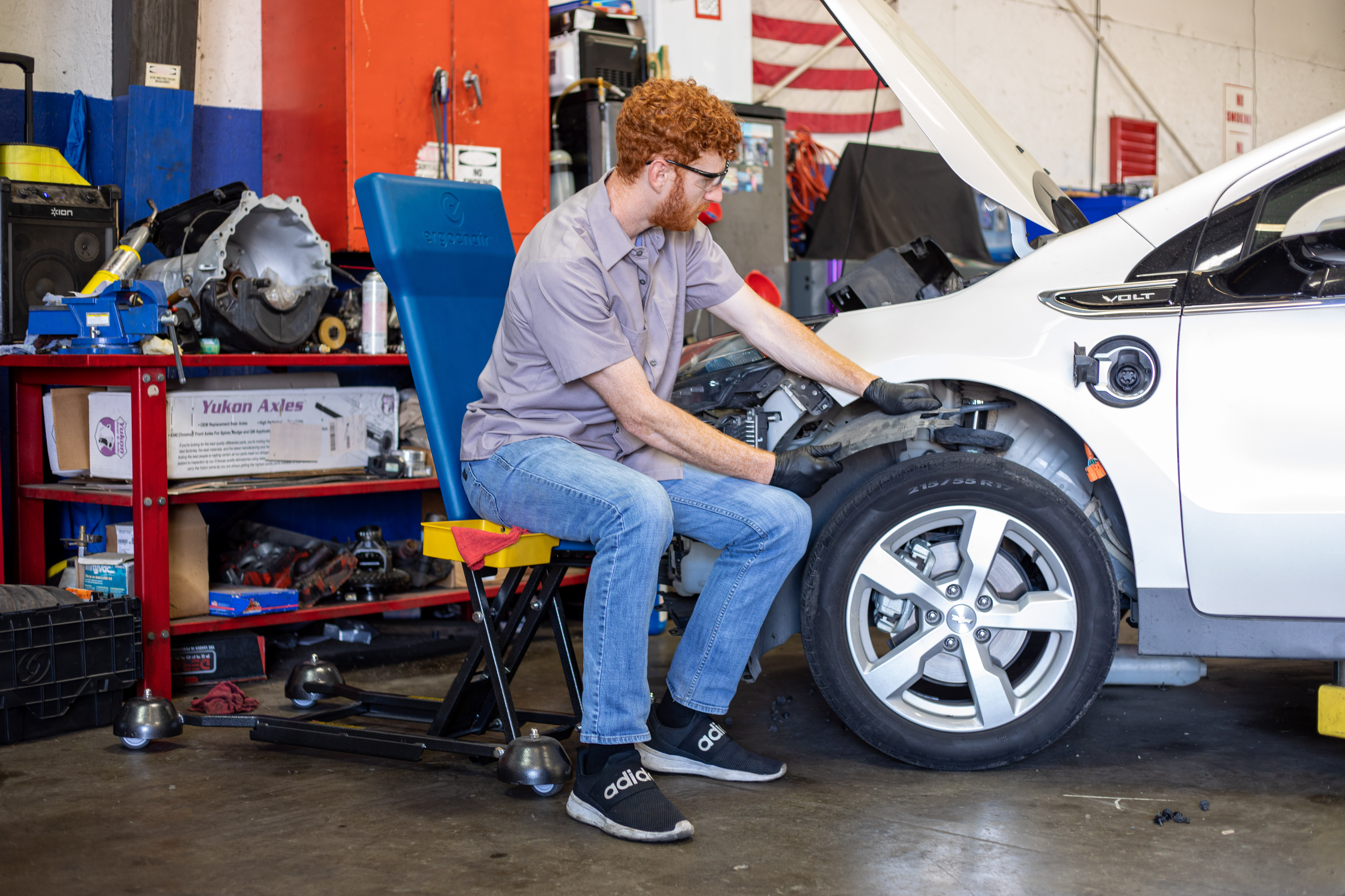 Person sitting in a blue adjustable work seat while working on a car's wheel well